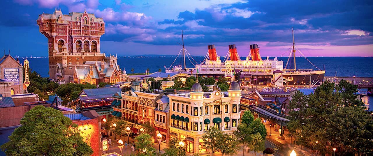Tokyo DisneySea’s waterfront buildings illuminated at dusk beneath a blue and pink sky