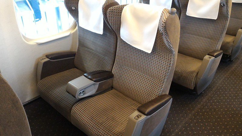 Wider gray upholstered seats with broad armrests inside a Shinkansen Green car