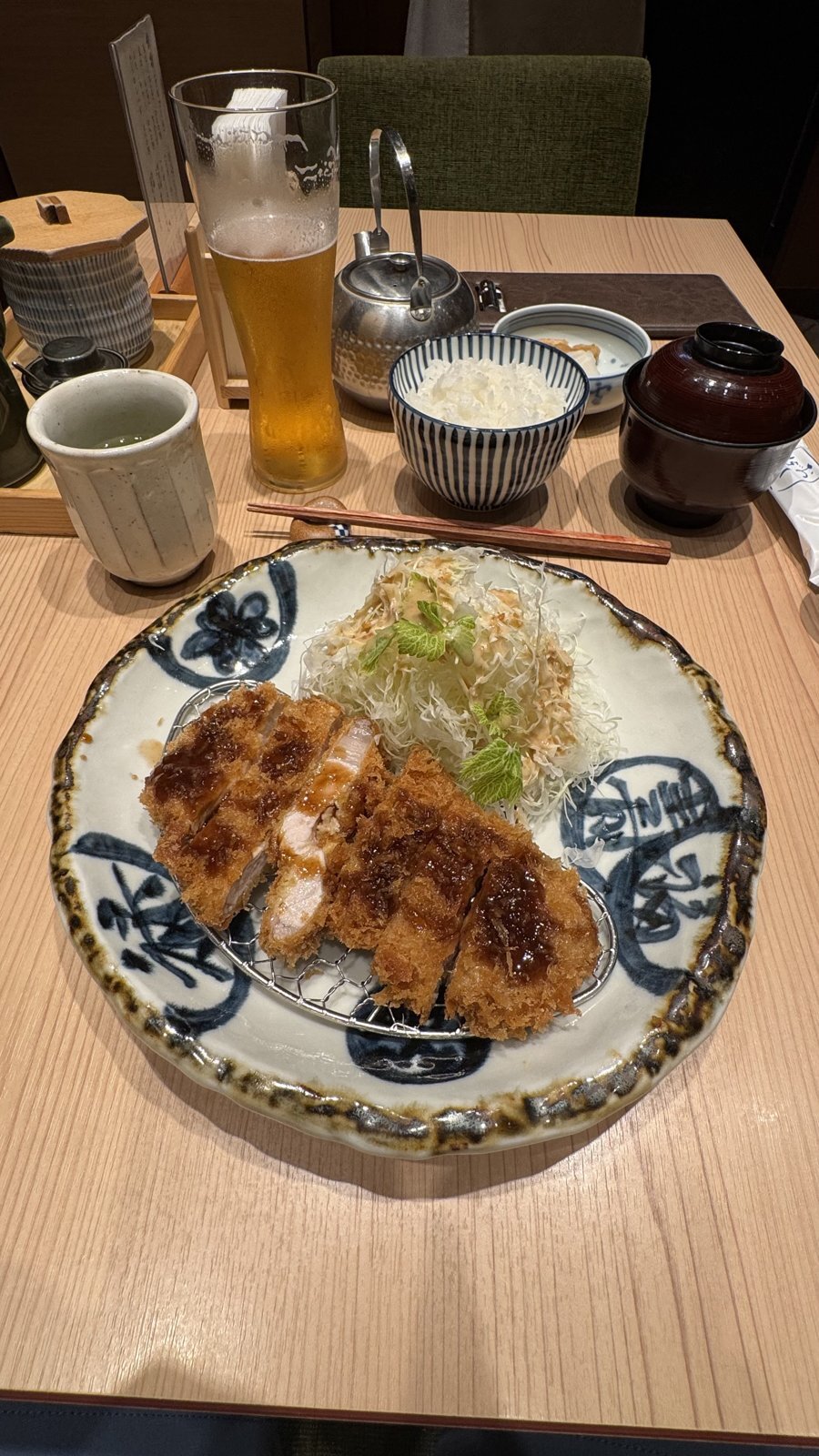 A tonkatsu meal with golden pork cutlets, shredded cabbage, rice, soup, and a glass of beer