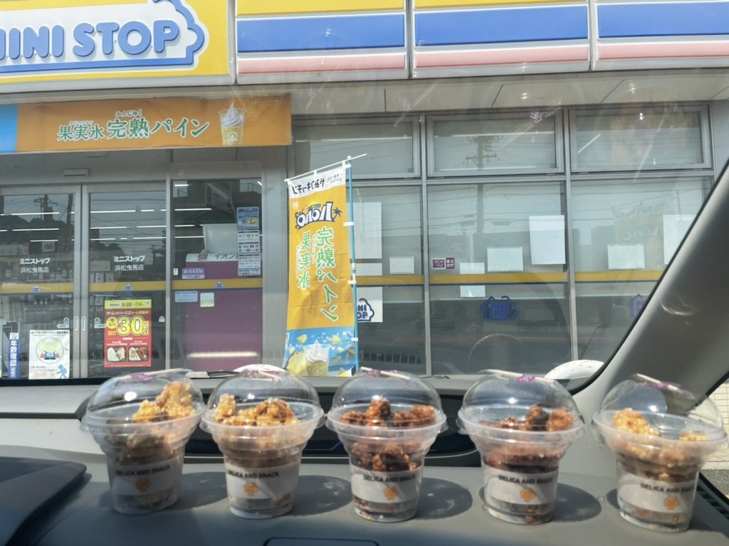 A MINISTOP storefront viewed through a car windshield, with cups of food on the dashboard